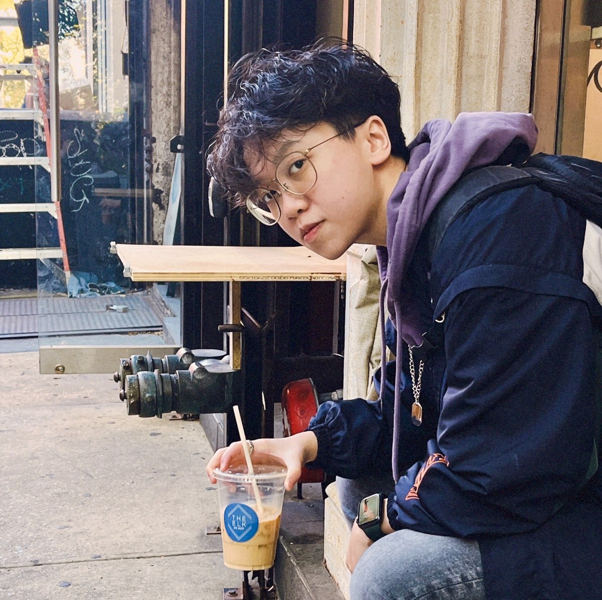 Melvin sitting outside a workshop in New York, holding an iced coffee.